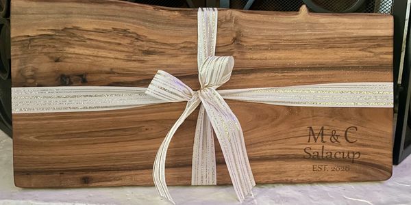 Wooden board engraved with "M&C Salacup EST. 2026" and tied with a glittery white ribbon.