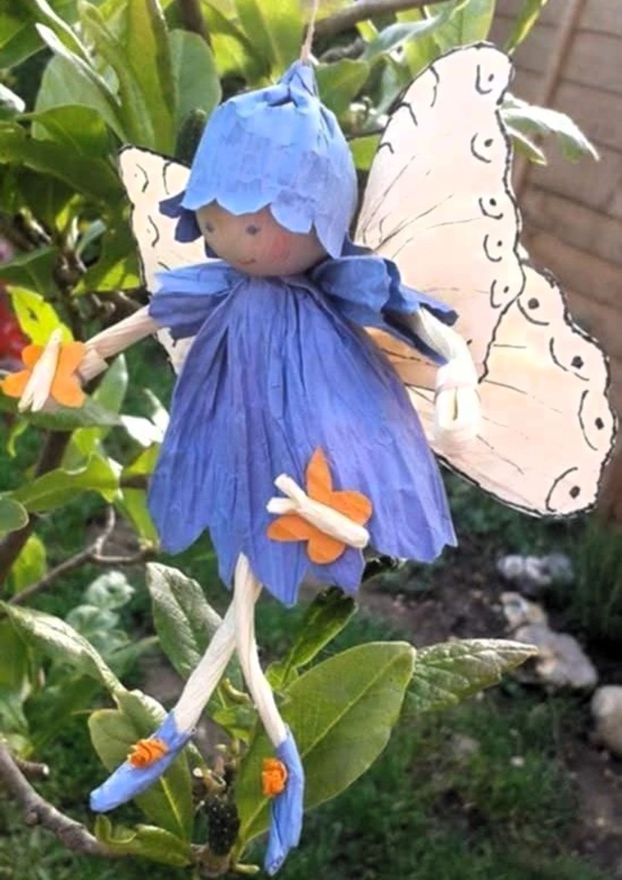 A handmade fairy doll with blue dress and wings hanging on a plant.