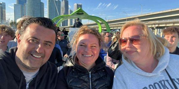 Three people smiling outdoors with city buildings in the background.