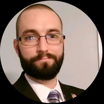 Man with glasses and beard wearing suit and tie.