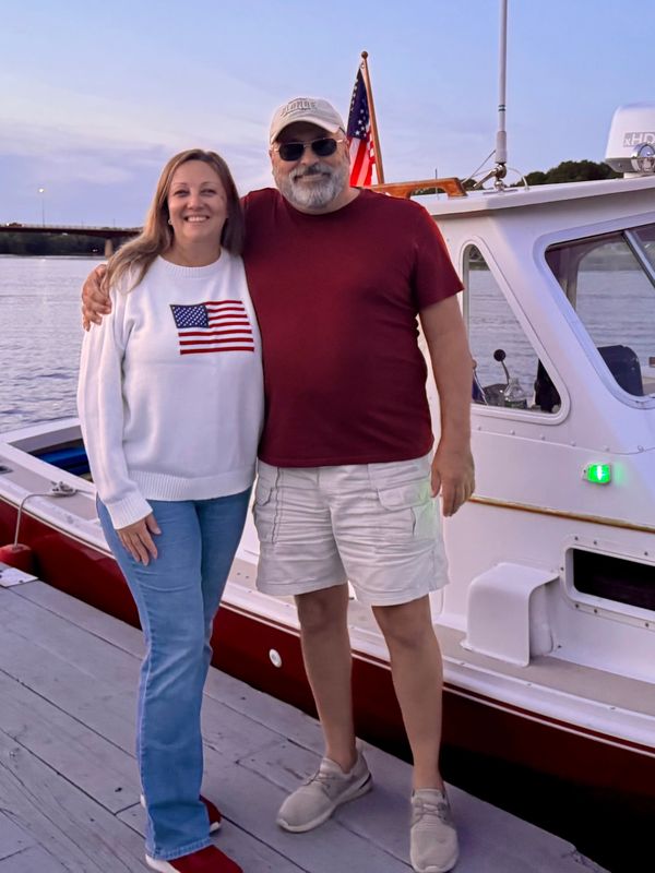 Couple posing happily by a boat at sunset.