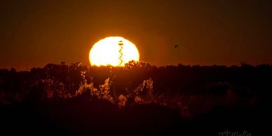 Close up of the sun rising behind a fire tower with a bird flying. By TJ Waller Photography
