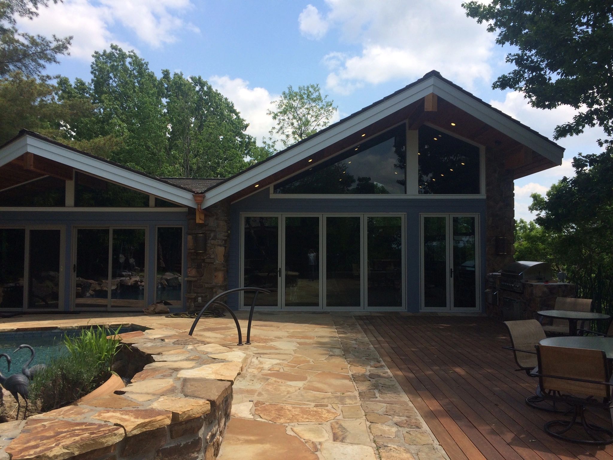 Modern house with large glass windows and a stone patio by the pool.