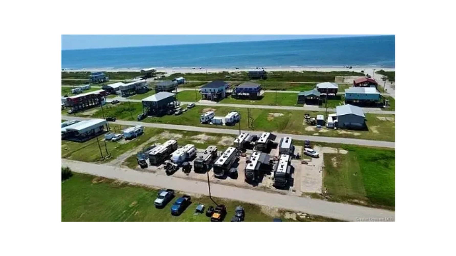 A coastal neighborhood with houses and parked RVs near the ocean.