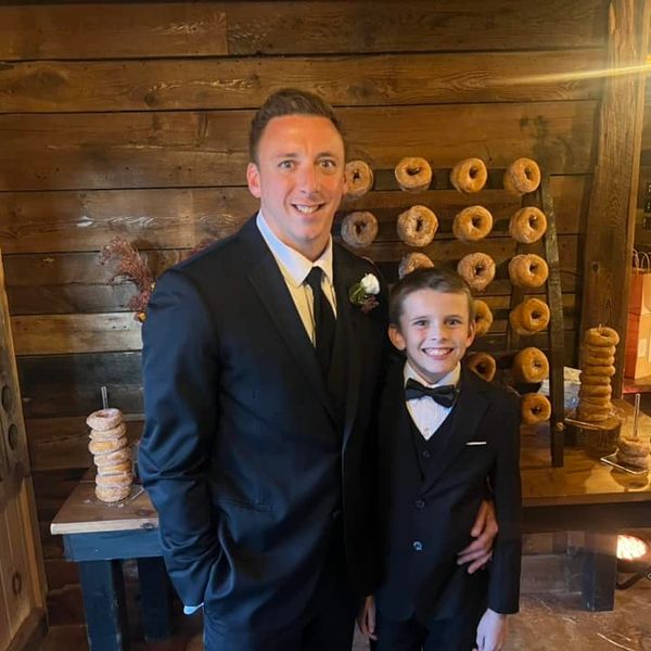 Two males in suits smiling with a donut wall behind them.