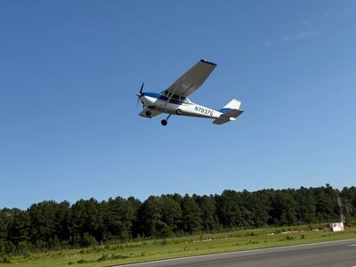 Small single-engine airplane flying above a runway on a clear day.