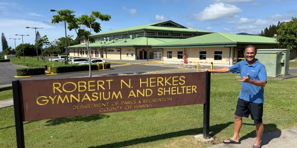 Man standing next to Robert N. Herkes Gymnasium and Shelter sign in Hawaii.