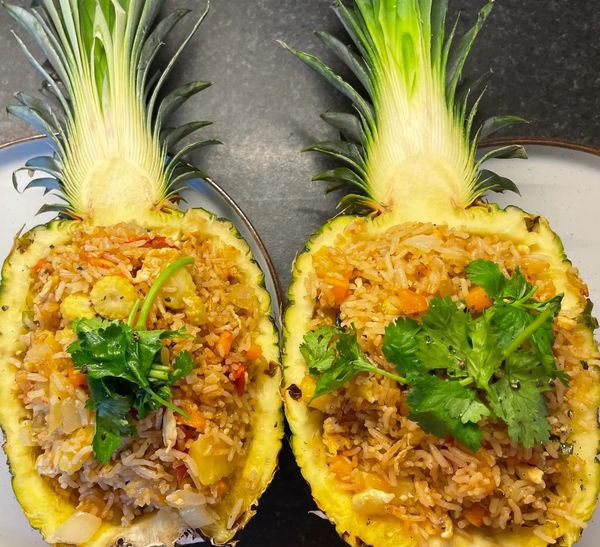 Fried rice served in halved pineapples with cilantro garnish.
