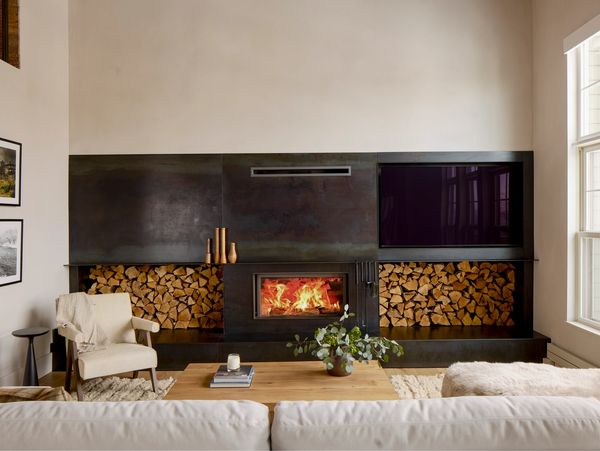 Modern living room with a fireplace, stacked firewood, and a TV.