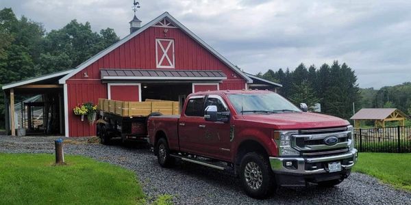 Red Ford truck parked in front of a red barn with a trailer attached.