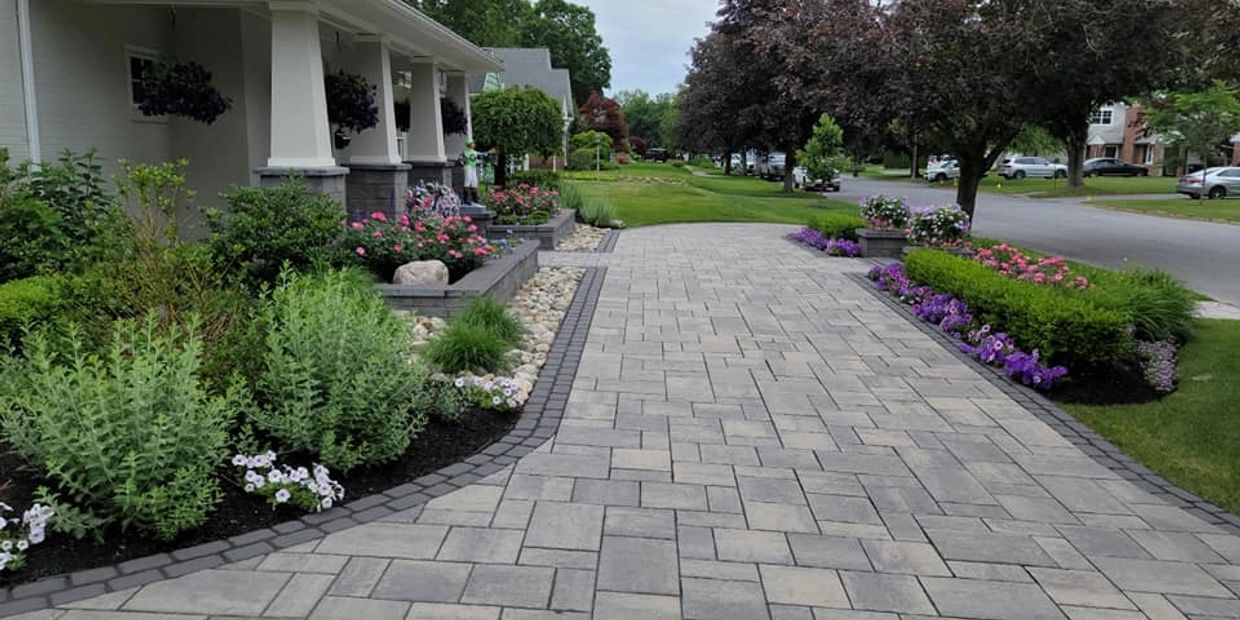 A paved driveway with flower beds on both sides in a suburban neighborhood.