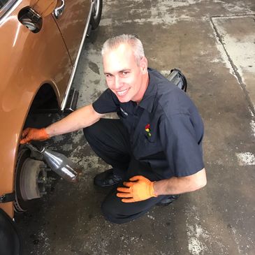 Mechanic smiling while working on a car wheel in a garage.