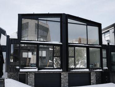 Modern black-framed house with large windows and snow-covered roof.