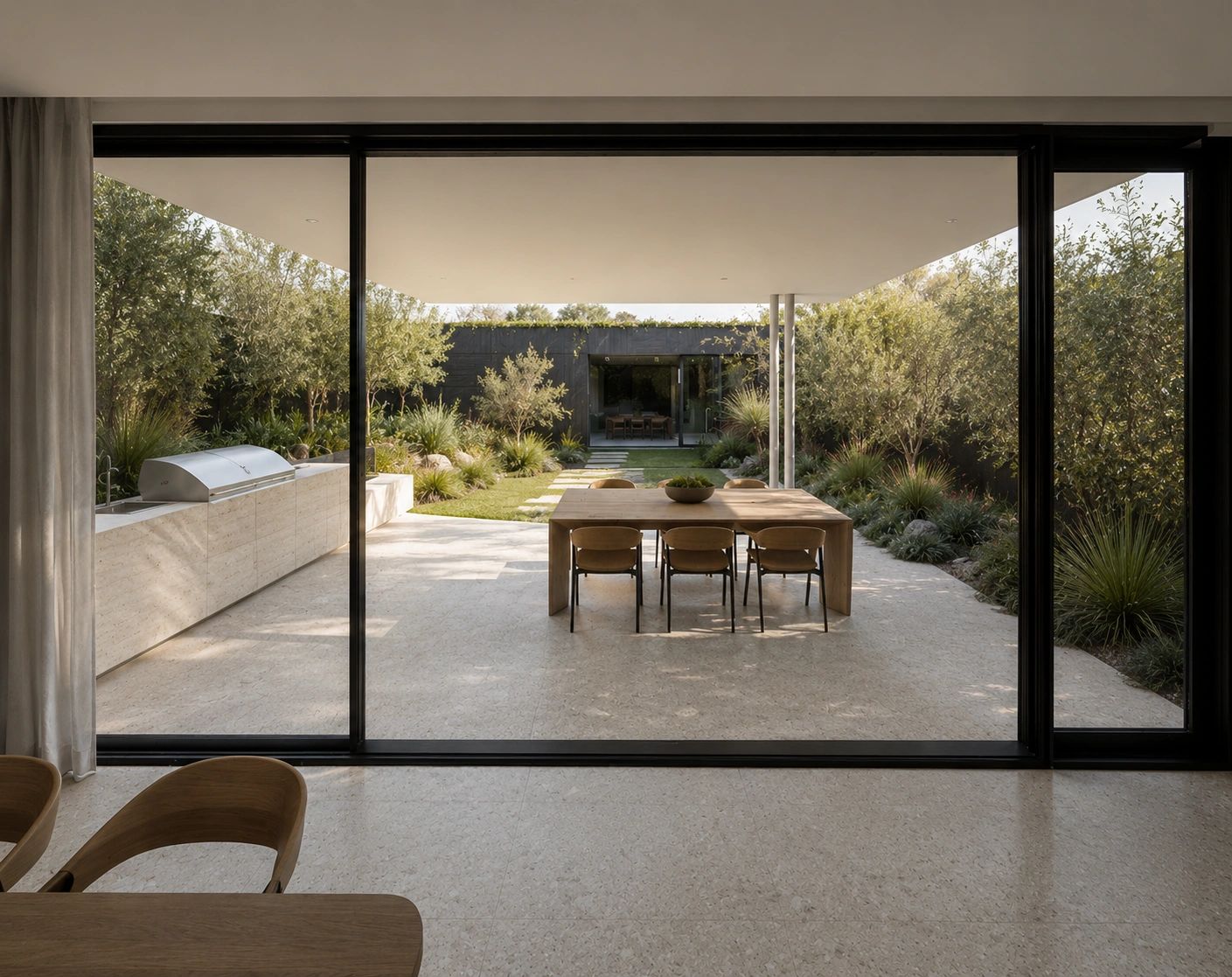 Modern outdoor patio with dining area and built-in grill surrounded by greenery.