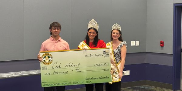 Three people, two women with crowns, holding a large check for $1,000.