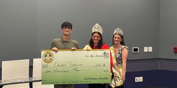 Three people holding a large $1000 check, two women wearing crowns and sashes.