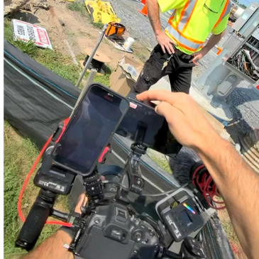 Person operating a camera with two smartphones attached at a construction site.