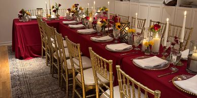 Elegant dining table with red tablecloth and golden chairs set for a formal event.