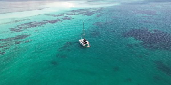 Sailboat anchored in clear turquoise ocean waters with visible coral reefs.