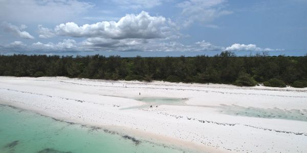 Pristine white sandy beach with turquoise waters and a cloudy blue sky.
