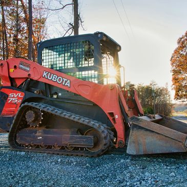 Kubota compact track loader parked on gravel at sunset.