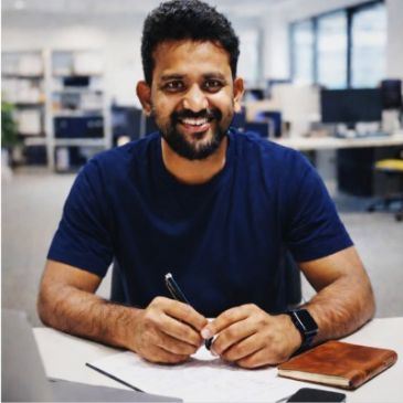 Man smiling while writing at a desk in an office.