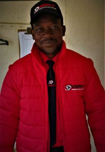 Man wearing a red jacket and matching cap with logos.