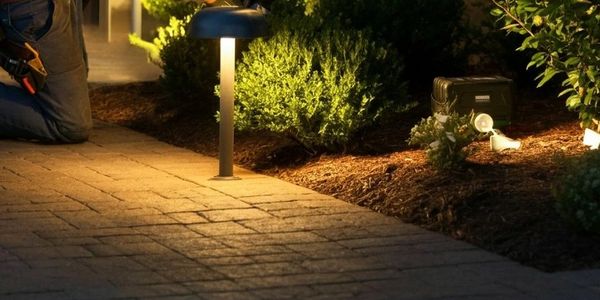 A technician installs outdoor landscape lighting at night by a garden path.