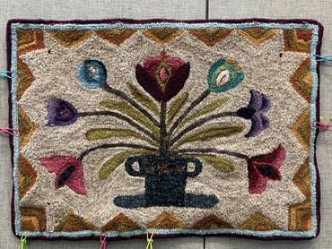 Handcrafted rug with colorful floral design in a pot.