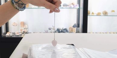 A person holding a heart-shaped pendulum over a book.
