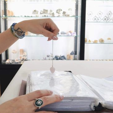 Person holding a pendulum over an open book or binder, possibly for divination or dowsing.