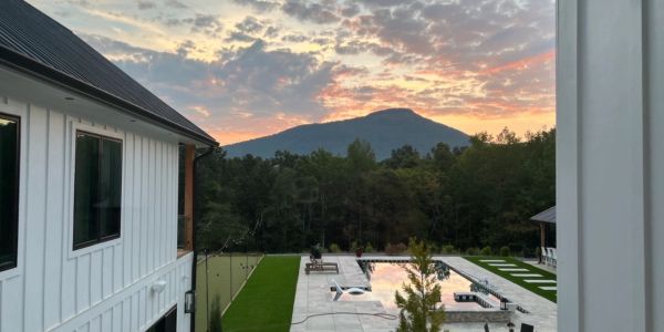 Sunset over a modern house with a pool and mountain in the background.