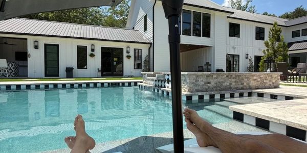 Two people relaxing by a modern pool with a white house in the background.