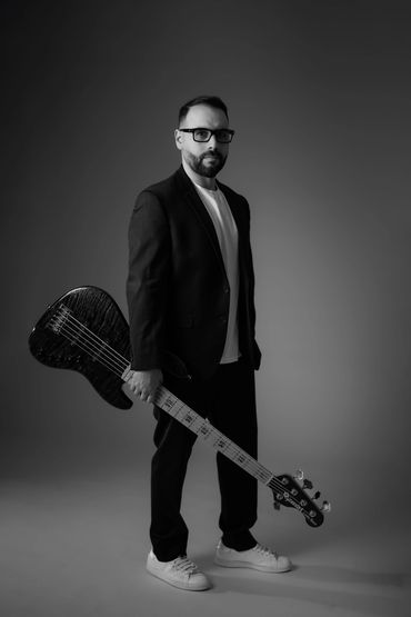Man in glasses holding a bass guitar, dressed in black and white.