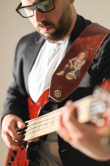 Man playing a bass guitar with a custom leather strap featuring a cartoon girl.