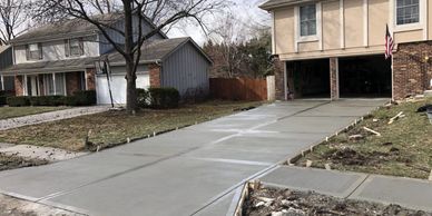 Freshly poured concrete driveway leading to a garage in a suburban neighborhood.