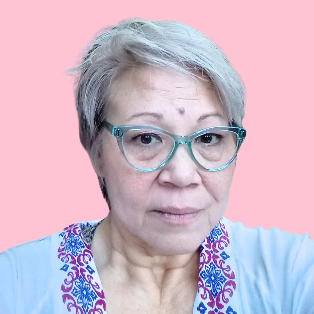 Elderly woman with short gray hair and turquoise glasses against a pink background.