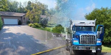 A blue dump truck parked on a residential driveway with trees in the background.
