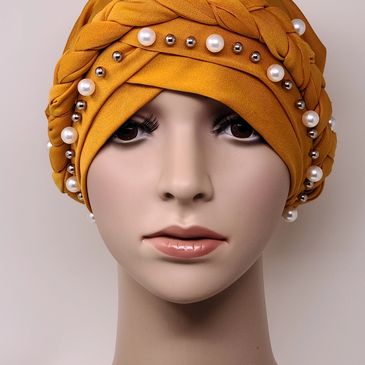 Mustard yellow braided turban with pearl and metallic studs on a mannequin. Elegant and stylish.