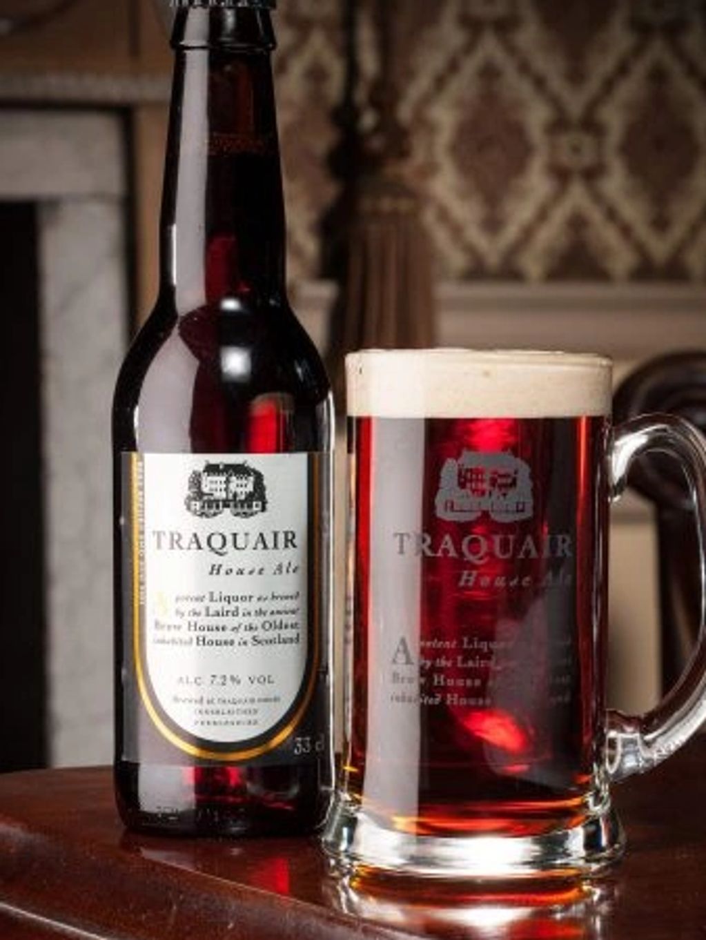 A bottle and glass of Traquair House Ale on a wooden table in a cozy setting.