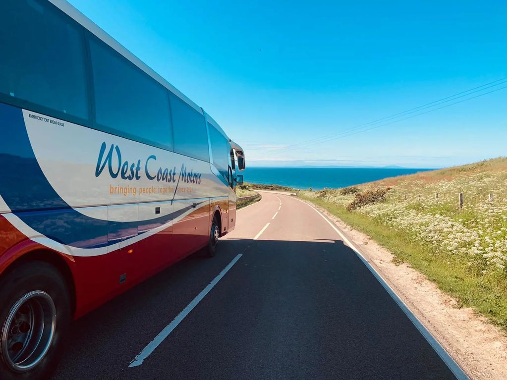 Bus driving on coastal road under clear blue sky.