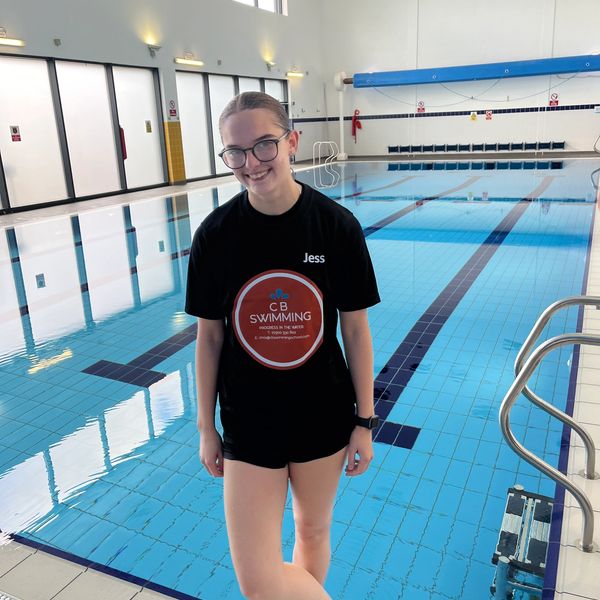Young woman with glasses standing by an indoor swimming pool.
