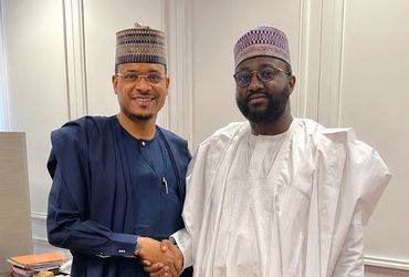 Two men in traditional Nigerian attire shaking hands indoors.