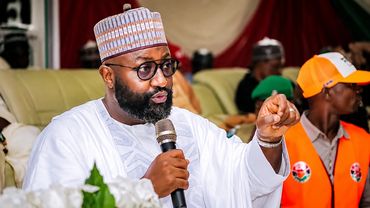 Man in traditional attire speaking into a microphone at an event.