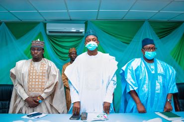 Four men in traditional attire wearing face masks at a meeting.