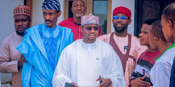 Engr. Ayuba Dauda Katagum, the SDP gubernatorial candidate for Bauchi State, standing in white traditional attire while consulting with community members and campaign supporters.
