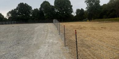 A fence dividing a gravel area and a dirt field under a cloudy sky.