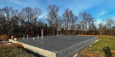 Concrete foundation slab for a building surrounded by trees under a blue sky.