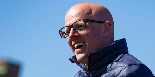 Smiling bald man wearing glasses and a blue jacket outdoors.