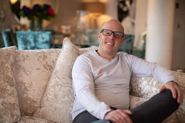 Smiling man in glasses sitting on plush sofa indoors.